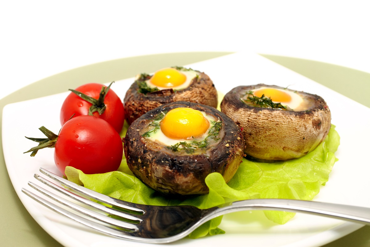 Ouă ochiuri în ciuperci pe foi de salată verde, alături de roșii proaspete