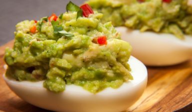 Două ouă umplute cu cremă de avocado și ardei pe un platou de lemn