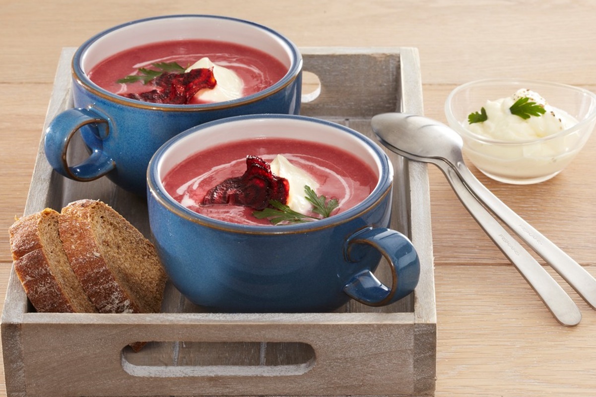 Două porții de Supă cremă de sfeclă roșie cu smântână în două boluri albaste așezate într-o tavă de lemn