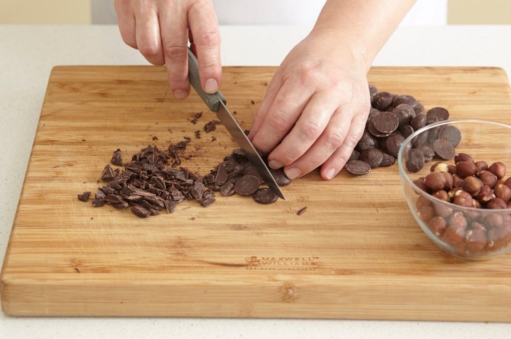 Pasul de mărunțire a ciocolatei cu un cuțit, pe un tocător de lemn