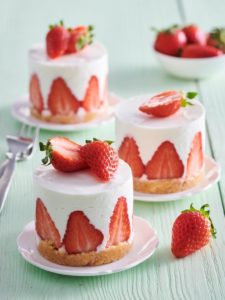 Trei porții de mini cheesecake cu căpșuni, pe farfurii micuțe, albe
