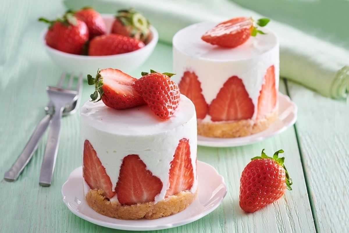 Trei porții de mini cheesecake cu căpșuni, pe farfurii micuțe, albe