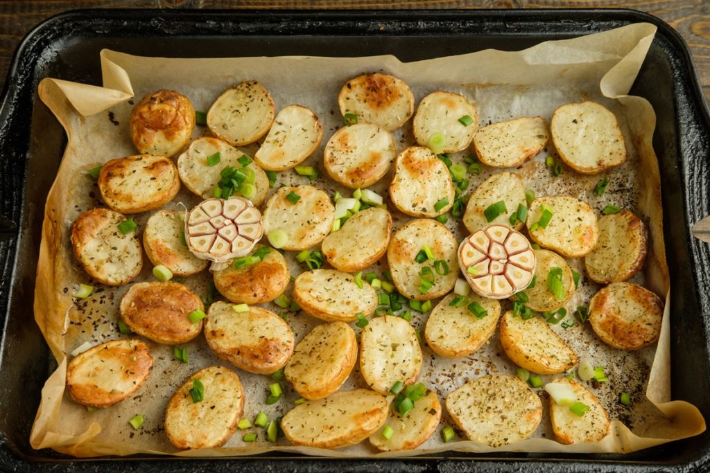 Tavă cu rondele de cartofi și de usturoi, coapte și presărate cu ceapă verde