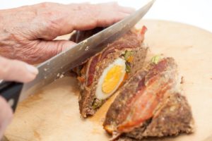 Rulada de carne cu ouă în felii de bacon se feliază cu un cuțit