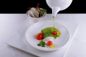 Supa cremă de mazăre turnată dintr-un ceainic alb în farfuria cu ingredientele pentru servit