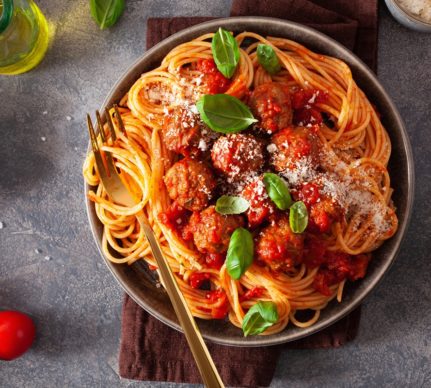 Porție de spaghete cu chiftele în sos de roșii, presărate cu parmezan răzuit