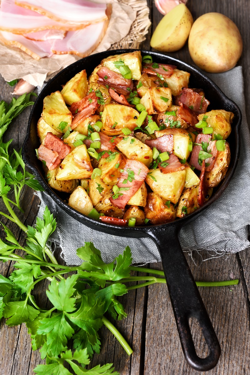 Bucăți de cartofi și de bacon în tigaie, presărate cu verdeață