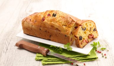 Chec sărat cu șuncă, măsline și cașcaval, feliat pe un platou alb, așezat lângă un cuțit, pe un ștergar verde