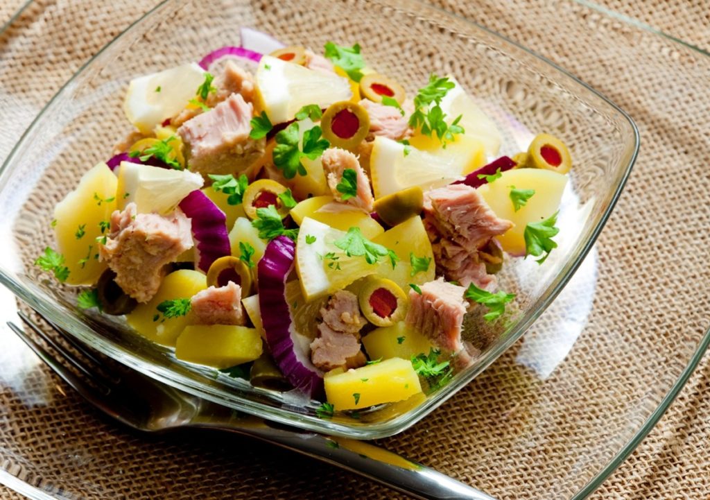 Salată de cartofi cu ton și măsline umplute cu ardei, într-un bol de sticlă cu furculiță