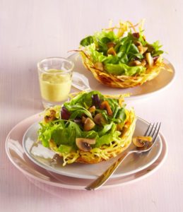 Două coșulețe din cartofi prăjiți cu salată și ciuperci, alături de un recipient cu sos de muștar