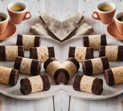 Rulouri de bezea cu alune și ciocolată pe două platouri albe, alături de patru cești maro cu cafea