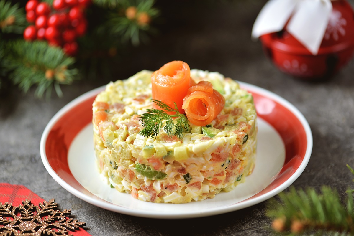 Salată de legume cu somon și maioneză, pe un platou rotund, adânc, într-un decor de iarnă