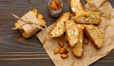 Biscotti toscani cu migdale sau Cantucci pe o hârtie de copt, alături de un borcan cu migdale și câțiva biscuiți împachetați