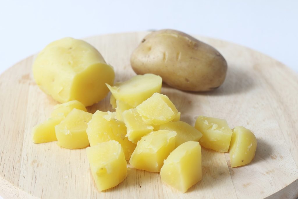 Cartofi fierți curățați și tocați în cuburi, unul necurățat