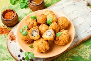 Ciuperci preparate pane pe un platou, două din ele secționate, alături de un vas cu sos și un borcan cu condimente