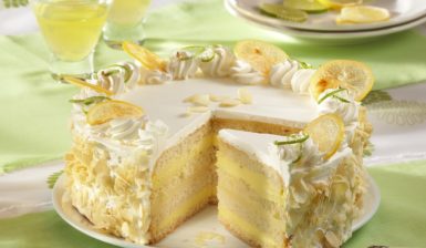 Tort cu aromă intensă de lămâie porționat pe platou, alături de două pahare cu suc și o farfurie cu felii de lămâie