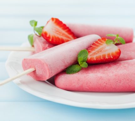 Cinci înghețate pe bețe așezate pe o farfurie și decorate cu căpșuni și mentă