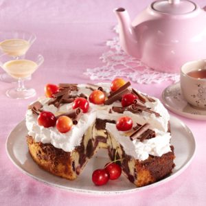 Tort cu blat bicolor și cireșe, cremă de frișcă și decor din ciocolată și cireșe, porționat pe platou, alături de un ceainic, o ceașcă de ceai și două pahare cu lichior