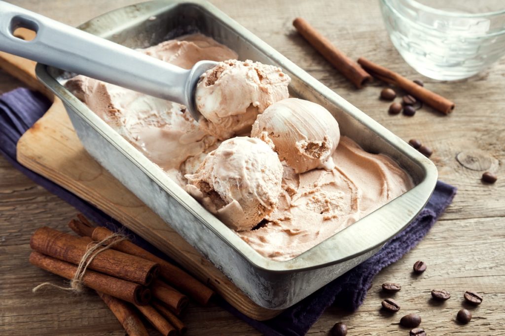 Trei cupe de înghețată de cafea cu scorțișoară porționate cu lingura specială, în caserola cu restul de înghețată