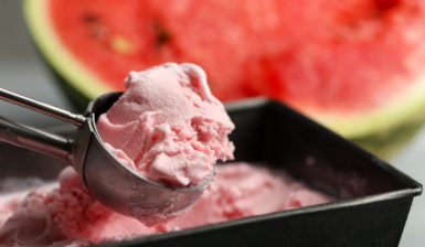 Înghețată de pepene roșu într-o caserolă cu lingură de inox, alături de o felie de pepene roșu