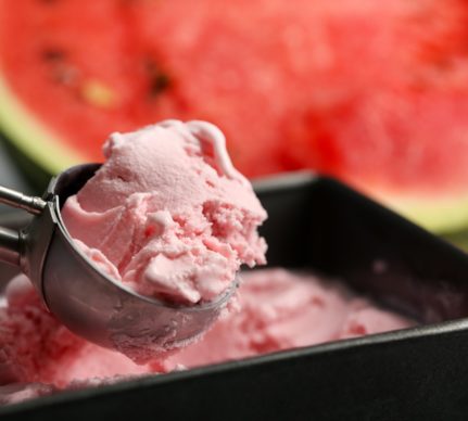 Înghețată de pepene roșu într-o caserolă cu lingură de inox, alături de o felie de pepene roșu