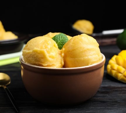 Trei cupe de înghețată în bol, alături de un mango secționat în cuburi