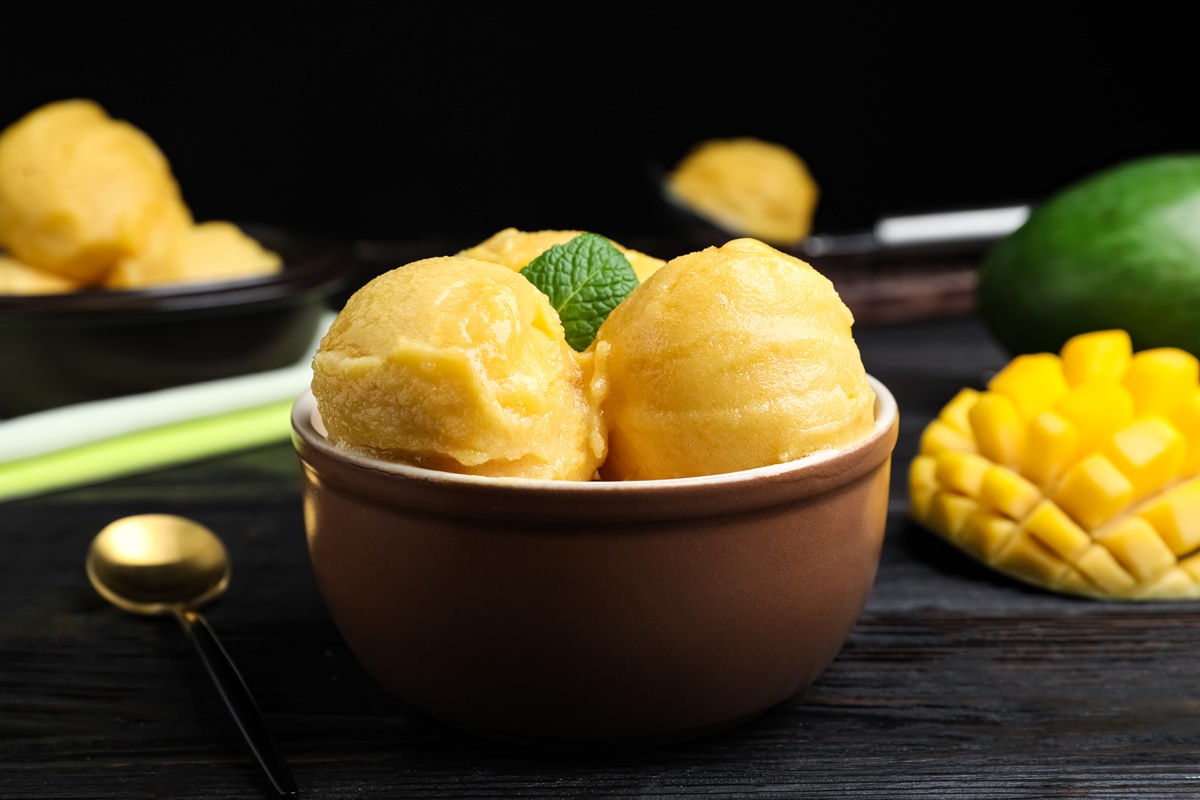 Trei cupe de înghețată în bol, alături de un mango secționat în cuburi