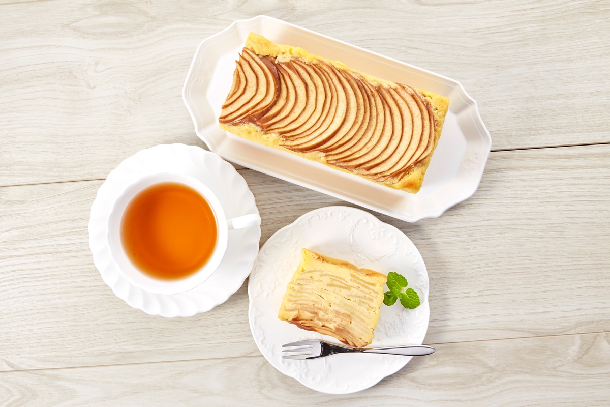 Prăjitură cu mere pe un platou oval și o porție pe farfurie, alături de o ceașcă cu ceai