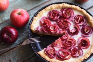 Tartă cu trandafiri din mere și cremă de vanilie secționată într-o tigaie cu furculiță