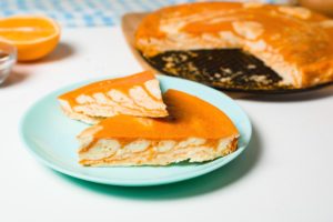 Două porții de cheesecake zebră cu dovleac și portocale pe o farfurie, alături de tava cu cheesecake