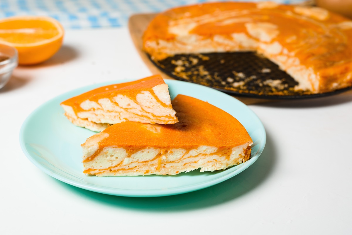 Două porții de cheesecake zebră cu dovleac și portocale pe o farfurie, alături de tava cu cheesecake