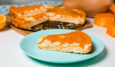 Porție de cheesecake zebră cu dovleac și portocale pe o farfurie, alături de tava cu cheesecake