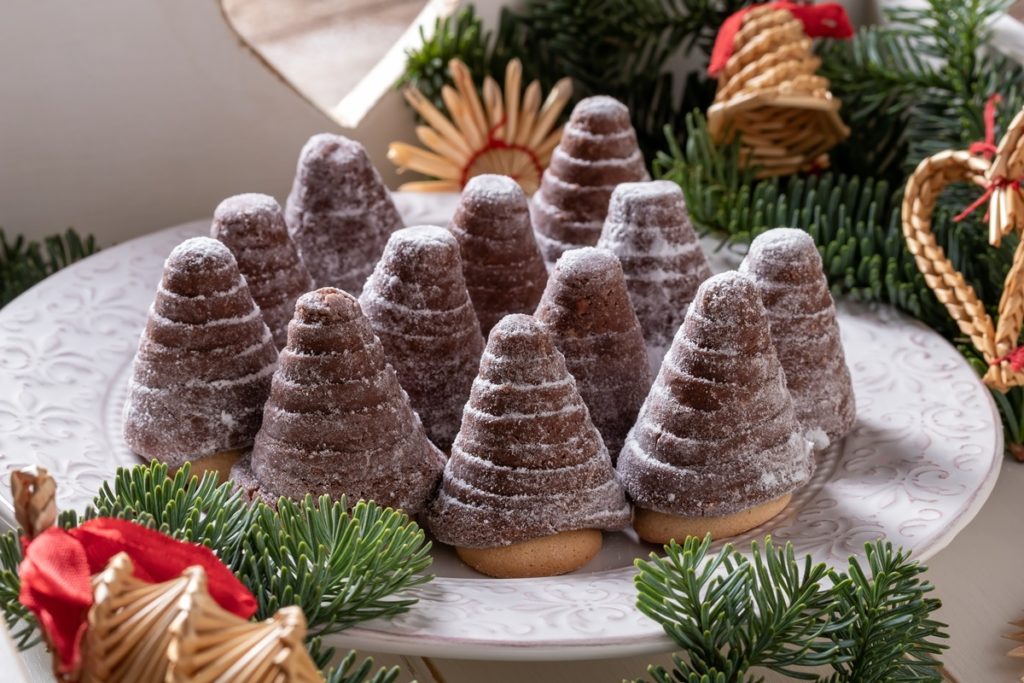 12 brăduți de Crăciun din biscuiți cu sos de ciocolată, pe o farfurie albă, într-un decor de sărbătoare