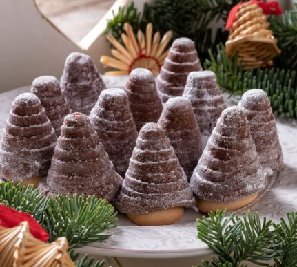 12 brăduți de Crăciun din biscuiți cu sos de ciocolată, pe o farfurie albă, într-un decor de sărbătoare