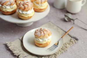 Un choux a la creme pe o farfurie cu furculiță, alături de platoul cu choux-uri