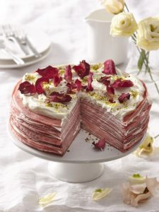 Tort de clătite red velvet cu cremă de mascarpone secționat pe un platou alb cu picior