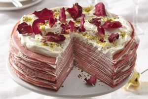 Tort de clătite red velvet cu cremă de mascarpone secționat pe un platou alb