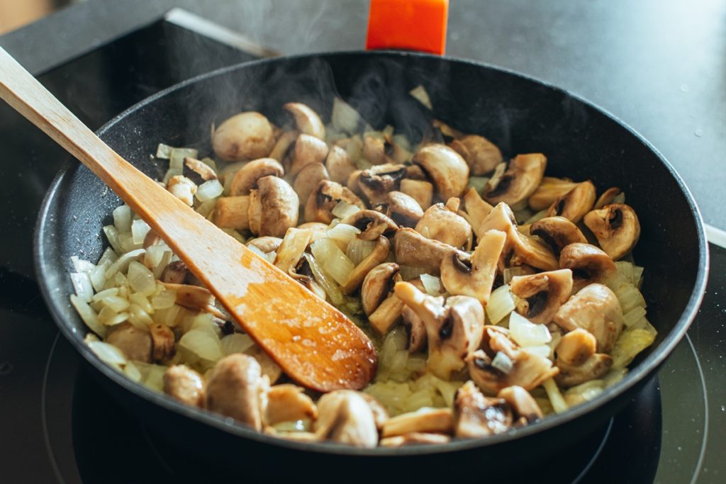 Ciuperci cu ceapă și usturoi amestecate cu o spatulă în tigaie