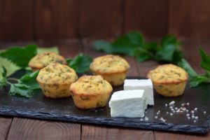 Muffins cu urzici și brânză pe un platou negru, alături de bucăți de brânză și urzici prpaspete, pentru gustări savuroase