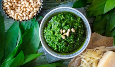 Pesto de leurdă cu parmezan în bol albastru, alături de leurdă, parmezan și semințe de pin