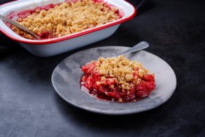 Crumble cu rubarbă și căpșuni în vas și în farfurie cu lingură