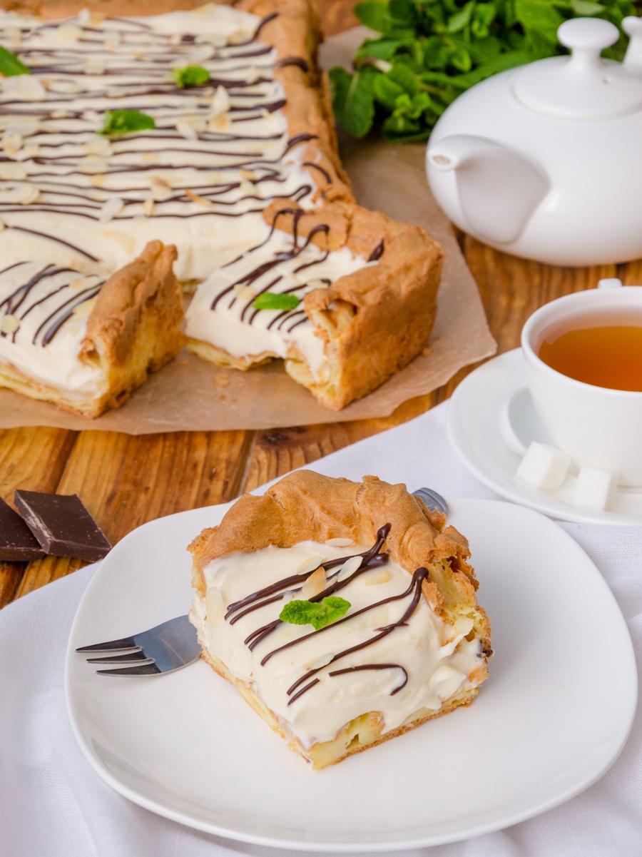 Prăjitură cu cremă bavareză și aluat opărit porționată, alături de un ceainic și o ceașcă cu ceai