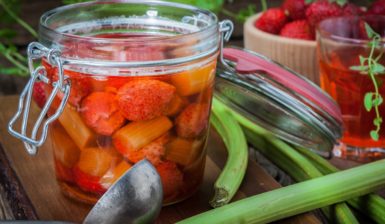 Compot de rubarbă cu căpșuni în borcan, un polonic, un bol cu căpșuni și tulpini de rubarbă