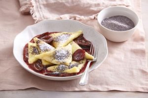 Bol cu ravioli de cartofi cu gem de prune și prune în sos caramel, alături de un bol mai mic cu zahăr, mac și scorțișoară