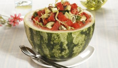 Salată de pepene roșu cu avocado și castraveți, decorată cu frunze de andive și semințe, în cupă de pepene roșu, alături de lingură și furculiță