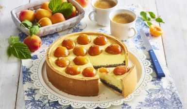 Cheesecake cu mac și caise proaspete porționat pe platou, alături de un bol cu caise și două cești de cafea