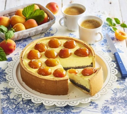 Cheesecake cu mac și caise proaspete porționat pe platou, alături de un bol cu caise și două cești de cafea