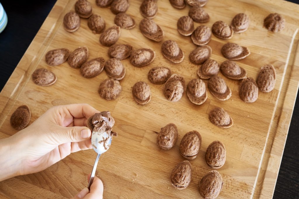 Femeie umplând cojile de nuci cu cremă de ciocolată, folosind o linguriță