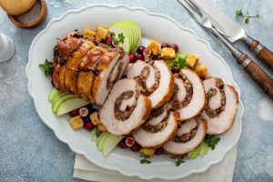 Ruladă de porc umplută cu nuci, pâine și merișoare pe un platou cu mere, merișoare și crutoane de pâine