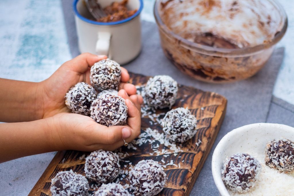 Bomboane de ciocolată cu biscuiți și nucă de cocos în mâini și pe un tocător